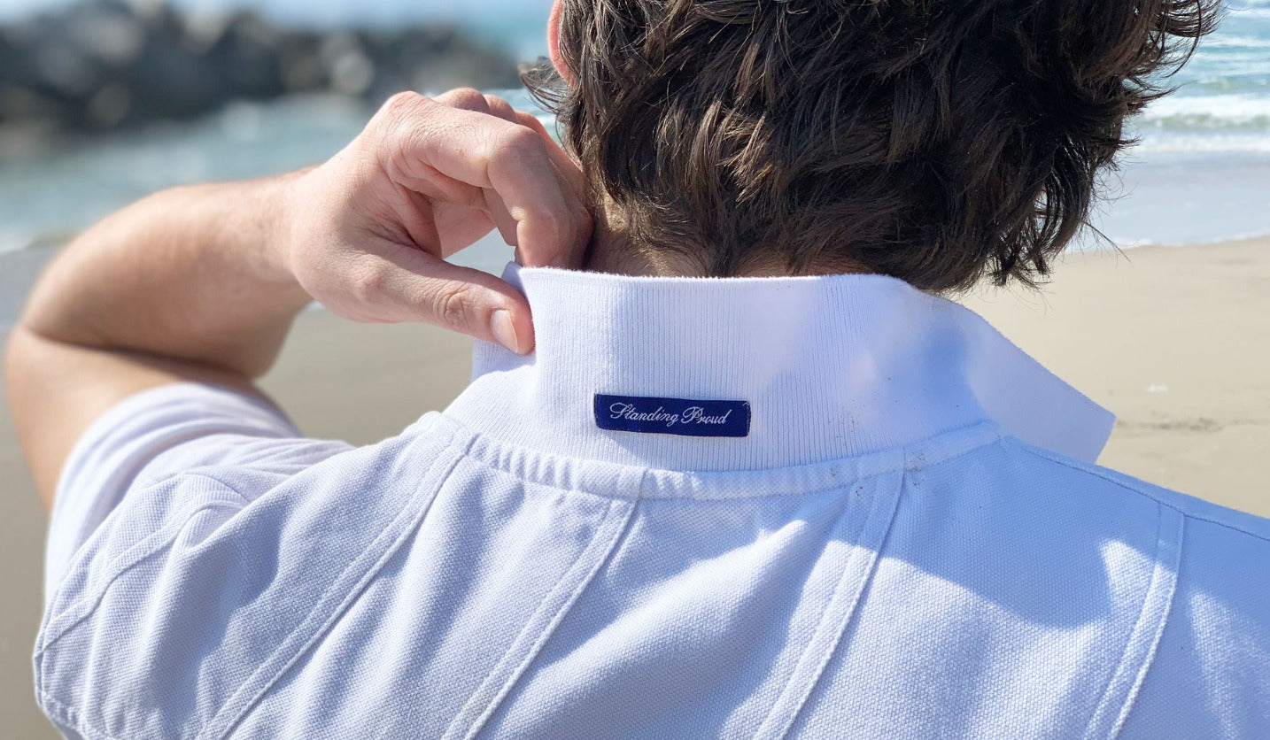 Man adjusting collar of a white polo shirt on a beach
